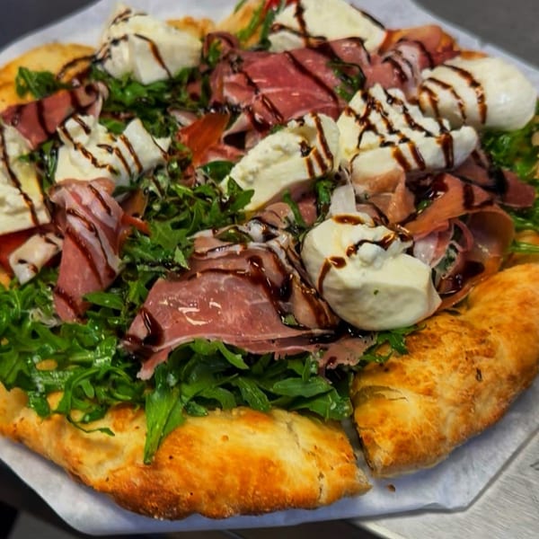 A gourmet pizza topped with prosciutto, fresh mozzarella, arugula, and balsamic glaze.